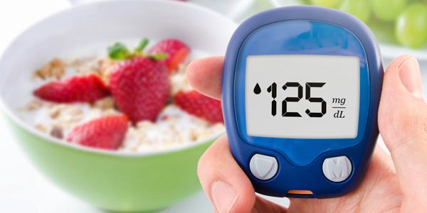 Eine Hand hält ein blaues Blutzuckermessgerät mit der Anzeige ‚125 mg/dL‘ vor einer Schale mit Joghurt und Erdbeerstücken.